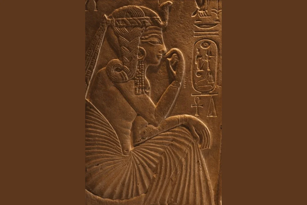 Ancient Egyptian relief carving of Pharaoh Ramesses II in a seated pose, shown in warm brown tones.