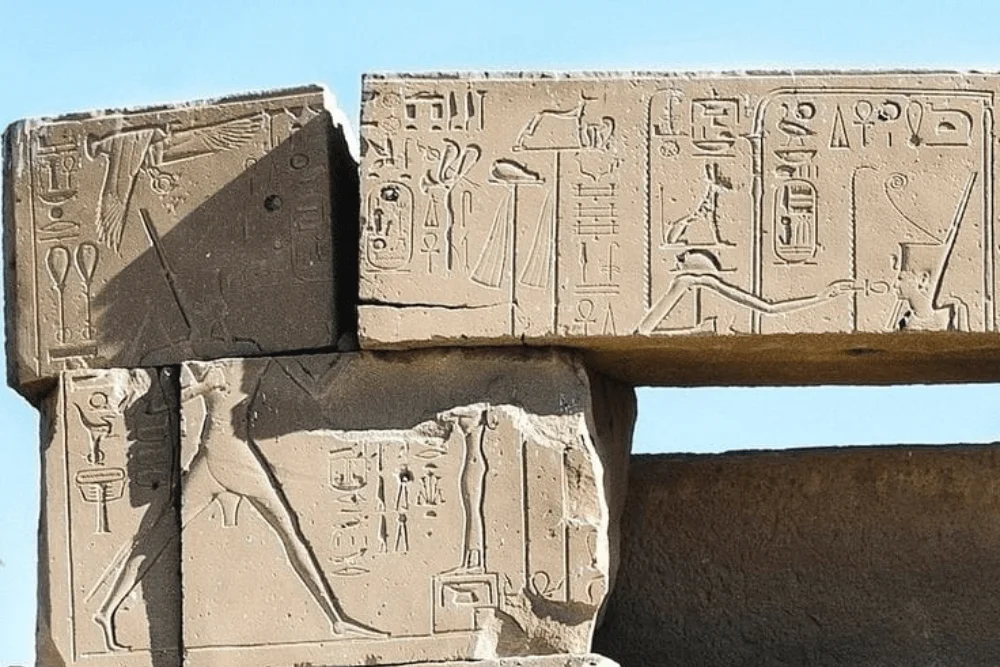 Ancient Egyptian temple lintel carved with hieroglyphs and royal figures, photographed against a blue sky.