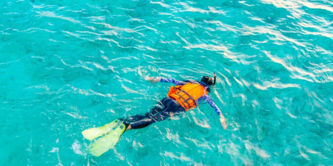 Snorkeler wearing an orange life vest and yellow fins in clear water.