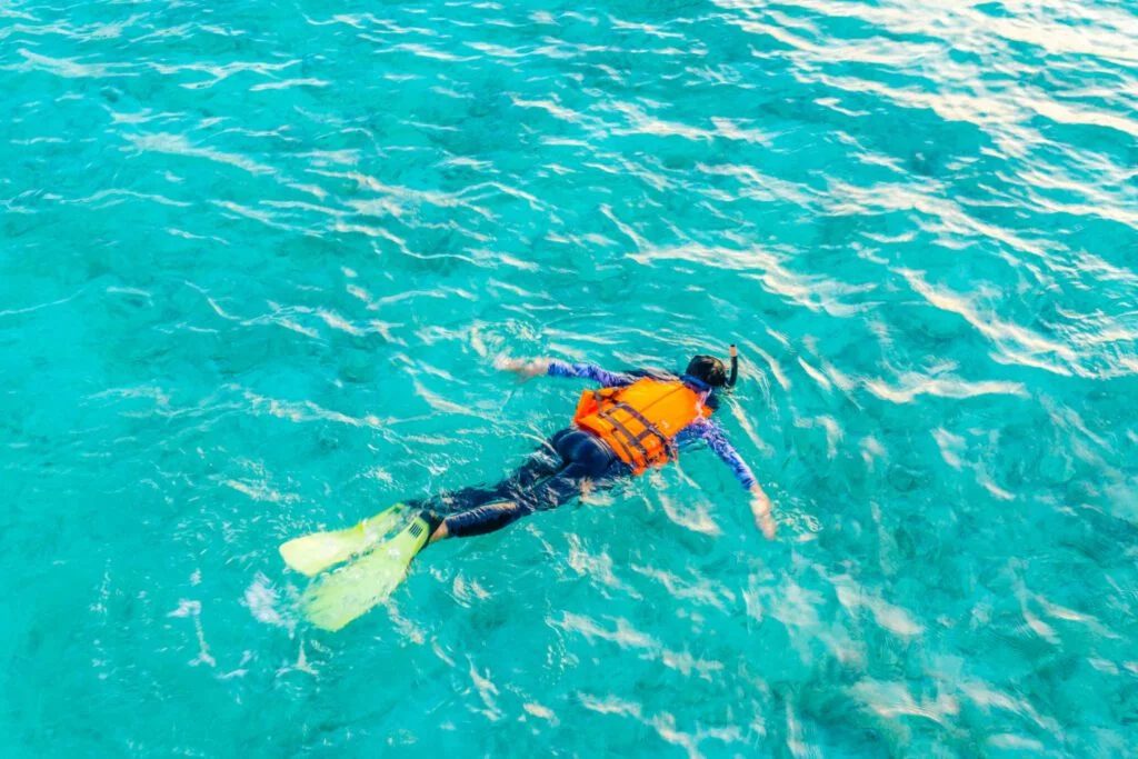Snorkeler wearing an orange life vest and yellow fins in clear water.