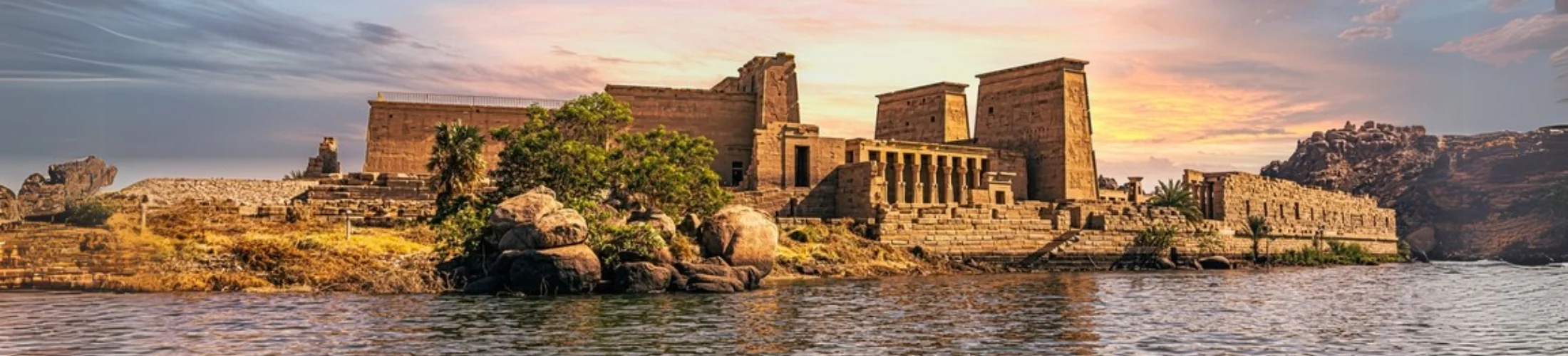 A scenic view of Philae Temple on the Nile River, illuminated by the golden light of sunset.