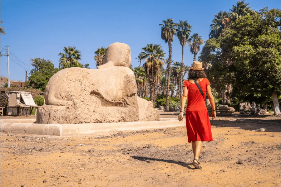 A visitor in red clothing beside a sphinx statue at an archaeological site.