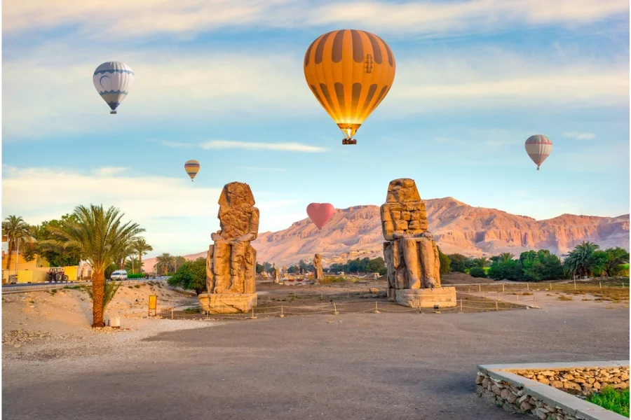 Hot-air balloons above a scene featuring the Colossi of Memnon.
