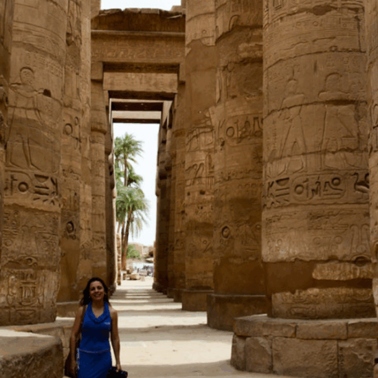 A tourist taking a photo inside Karnak Temple surrounded by ancient columns.